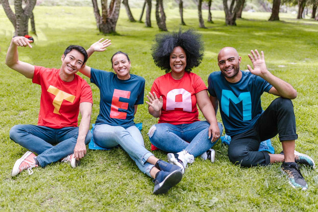 Multiracial team sitting on grass in park, wearing 'TEAM' shirts, showing unity.